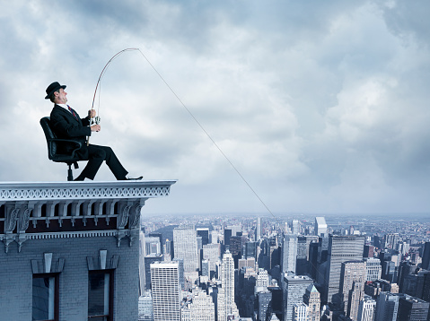 A businessman on top of a building fishing for business from the city below.