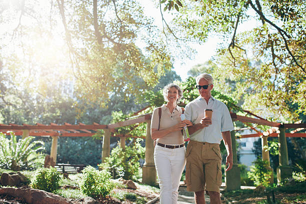 Couple of tourist walking through a park Portrait of couple of senior tourist walking through a park on a summer day. mature couple on a vacation. tourist couple candid travel stock pictures, royalty-free photos & images