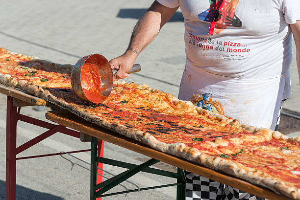 Guinnes World record pizza long 2 km Naples, Italy - May 18, 2016: pizza maker added tomato sauce to the longest pizza in the world on the Naples waterfront. Naples beat the Guinness world record for long pizza margherita circa 2 Km .The super pizza of about 1,850 meters, exceeding the previous record of 1,595 meters, reached June 20, 2015 at Expo in Milan. guinnes stock pictures, royalty-free photos & images