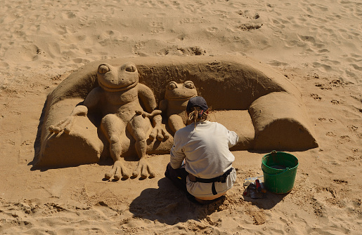 Cascais, Portugal - March 08, 2016:Woman making sand sculpture of Frog aitting on sofa on Cascais beach. 