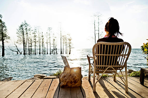 Young woman working on her laptop while sitting by the lake.