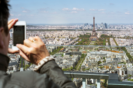 Cropped image of man photographing Eiffel Tower and cityscape. Male is taking picture of monument through mobile phone. He is visiting one of the most famous place in Paris.