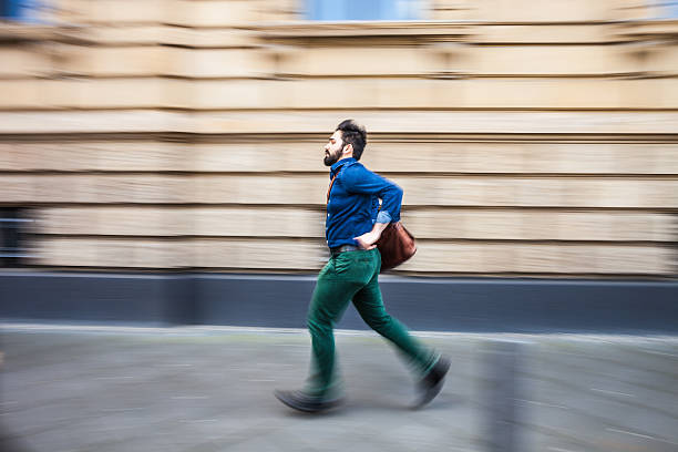 Business man outside the office building running on the sidewalk. He is wearing a formal and elegant grey suit.