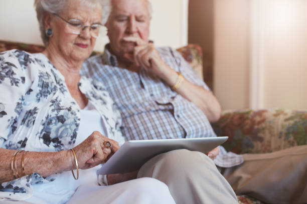 casal idoso em casa usando tablet digital - ipad senior adult facebook sofa imagens e fotografias de stock