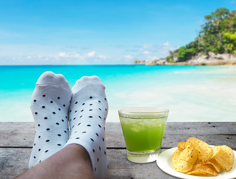 feet on wooden floor with glass of apple juice and potato chips over beach background, Relaxtion on vacation concept