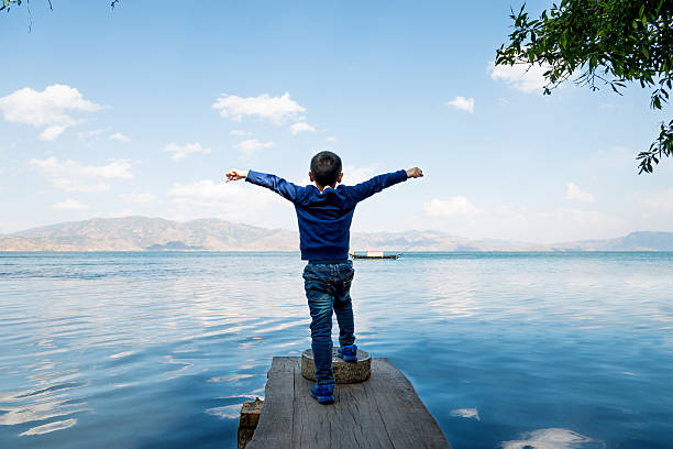 Little boy raising his hands on lakeside.