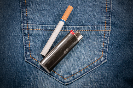 Pack of cigarettes and lighter in pocket of jeans. Closeup