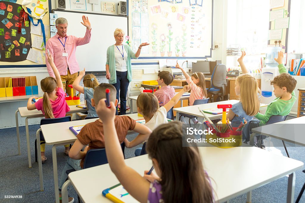 Classroom Discussion A group of young school children are sitting in a classroom with their hands raised waiting to have a discussion with the teachers. England Stock Photo