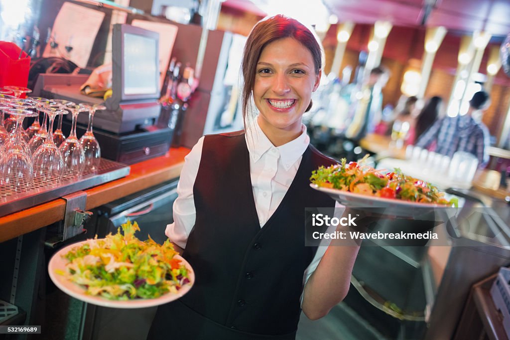 Pretty barmaid holding plates of salads Pretty barmaid holding plates of salads in a bar Waitress Stock Photo