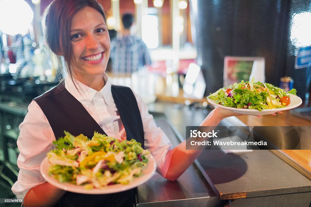 Pretty barmaid holding plates of salads Pretty barmaid holding plates of salads in a bar Food And Drink Industry Stock Photo