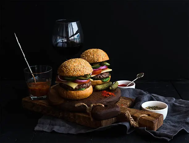 Photo of Fresh beef burgers on rustic wooden boards with glass of