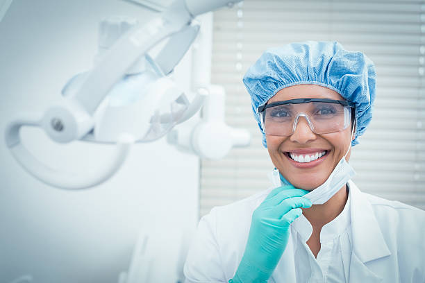 femmina dentista indossando cappellino chirurgico e occhiali di sicurezza - dentista foto e immagini stock