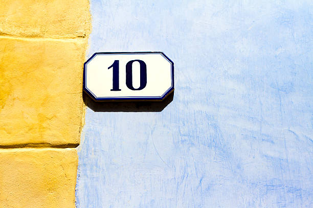 Blue and white vintage ceramic number 10 street address tile on a pretty Mediterranean blue and yellow wall with lots of copy space. Shot in Italy.