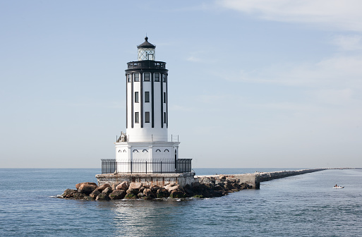 A beautiful lighthouse sits on a bank of rocks out in the middle of the ocean in Port of Los Angeles California at San Pedro. A little dingy hangs around to the right.