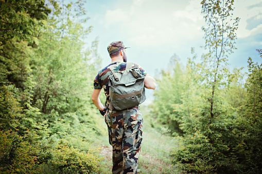 Soldier in the mountain forest alone, walks and caries a backpack. Rear view.