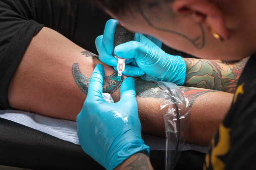 Close-up of Tattoo artist tattooing right arm of cauasian man