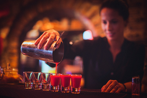 Close-up of a young female bartender pouring cocktail in a nightlife cocktail bar. Selective focus. Focus on foreground.