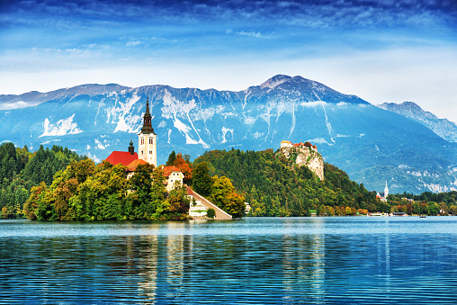 Lake Bled located in Slovenia Europe. There is a Church on the Island and ancient castle on top of a rock. Beautiful blue sky with dramatic cloudscape over the reflection in the Bled Lake. Story in such a beautiful sunny day on sunset. European Alps in the background.