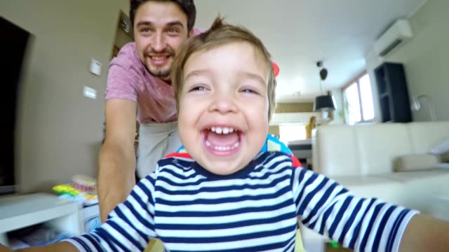 Point of view shot of a laughing father and his son sitting in the walker while being pushed across the apartment.
