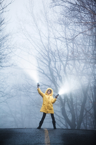 Teenager girl with flashlights walking in the haze, on the country road in the forest. Pennsylvania, Poconos
