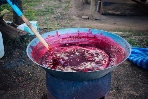 In Pai, Thailand a large heated pot boiling with red roselle fruits, also called rosella is being stirred.  