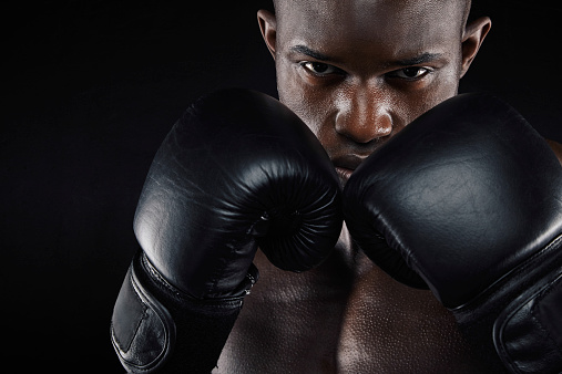 Portrait of a young male boxer in a fighting stance on black background. Young man doing boxing exercise.
