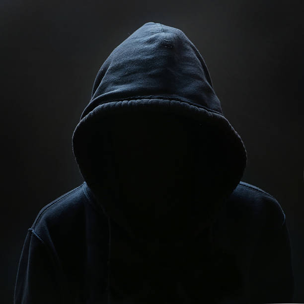 Unrecognizable person Unrecognizable person wearing hood against black background murderer stock pictures, royalty-free photos & images