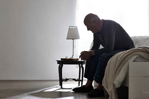 Elderly man sitting on bed looking serious - Indoors