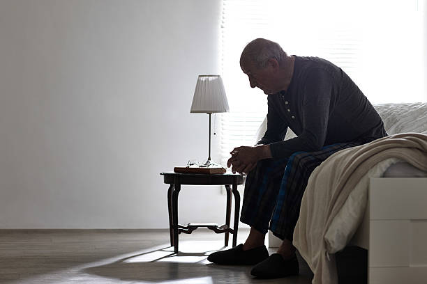 Elderly man sitting on bed looking serious Elderly man sitting on bed looking serious - Indoors old man depressed stock pictures, royalty-free photos & images