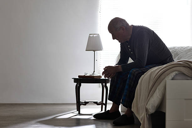 homem idoso sentado na cama olhando sério - loneliness solitude sadness depression imagens e fotografias de stock