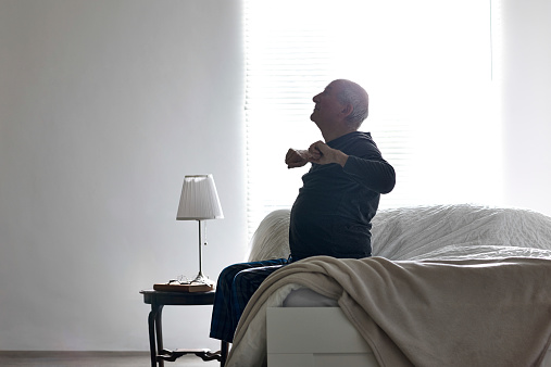 Senior man sitting on bed stretching his arms - Morning exercises