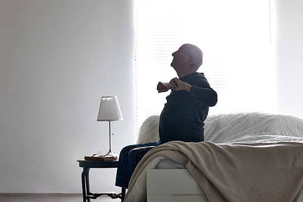 starszy mężczyzna siedzi na łóżku jego ramiona, rozciągająca się - therapy physical impairment disabled senior adult zdjęcia i obrazy z banku zdjęć