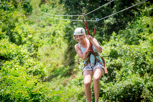 Beautiful happy woman riding a zip line in a lush tropical forest while on family vacation. Having fun and smiling with excitement