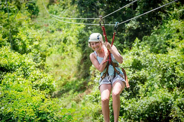 Beautiful happy woman riding a zip line in a lush tropical forest while on family vacation. Having fun and smiling with excitement