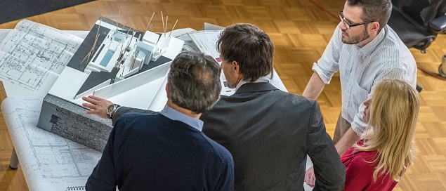 High angle view of architects and clients looking at an architectural model and plans.