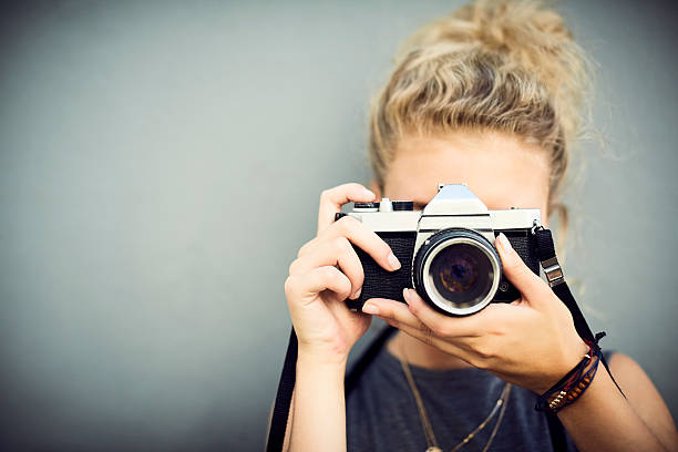 Close-up of woman using digital camera. Young female is adjusting lens while photographing. She is standing against wall.