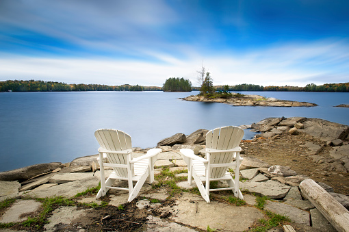 Two white Muskoka chairs facing the lake. Relaxing atmosphere during Fall season.