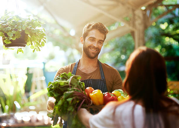 Personal service at it's best Shot of a man giving a customer a crate full of fresh produce at a farmer’s market market vendor stock pictures, royalty-free photos & images