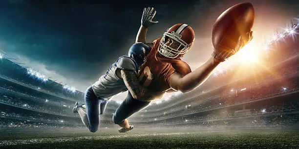 Image of an american football player being tackled by the opposite team player during the flight to touchdown. All players wear unbranded professional clothes. Action takes place in a generic outdoor football stadium under a cloudy dark sky with bright sun.