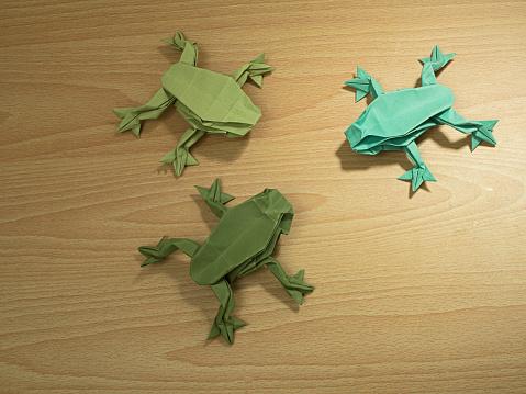 Three Origami Frogs on wooden desk background