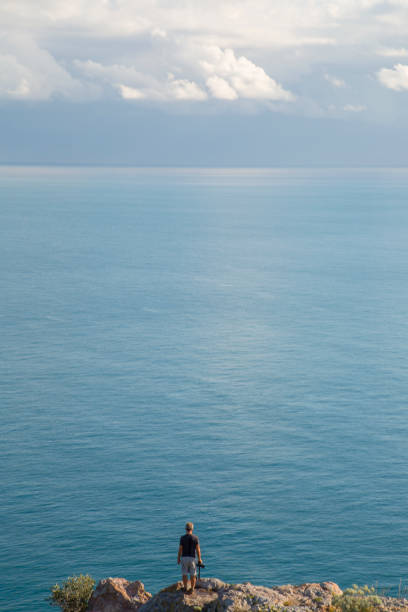 istock Man holds camera on bluff, looks out to sea 532309245