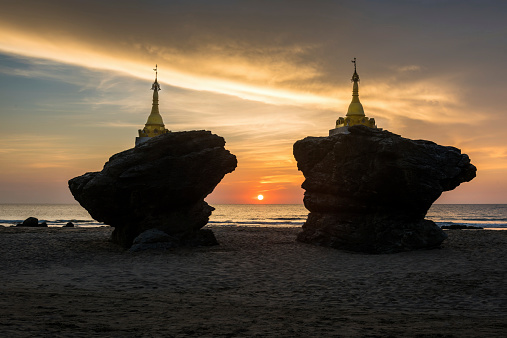 Sunset between two pagodas on natural rocks on the beach. Twin Pagoda Ngwe Saung Beach, Bay of Bengal, Burma - Myanmar, Asia