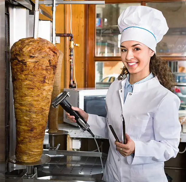 Photo of Professional  female cook with grilled meat on spit for kebab