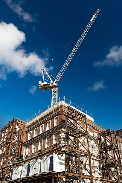 A dynamic view of a high-rise under construction in London, showcasing cranes and a visible steel truss framework. The geometric patterns of the structure contrast with the clear blue sky, emphasizing architectural development and urban growth