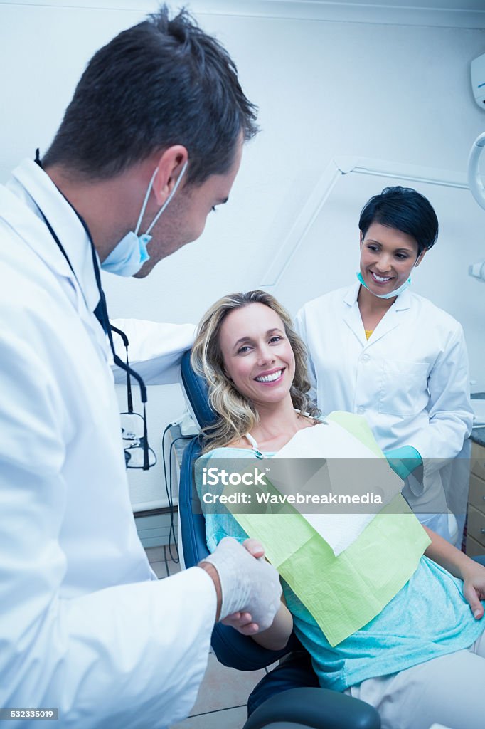 Dentist with assistant shaking hands Male dentist with assistant shaking hands with woman in the dentists chair Greeting Stock Photo