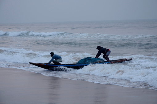 Orissa, India - December 30, 2014:  traditional Indian fishermen taking in their boat in the morning