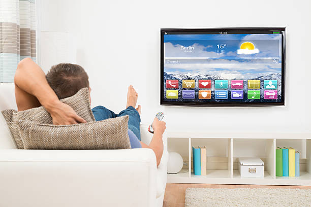 Man Using Remote Control In Front Of Television Young Man Lying On Sofa Using Remote Control In Front Of Television smart tv stock pictures, royalty-free photos & images