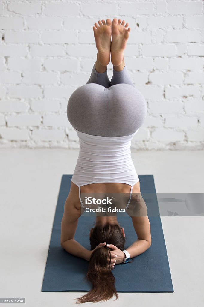 Yoga Indoors: preparation for Salamba Sirsasana Beautiful young woman with flower tattoo on her back working out indoors, doing yoga exercise on blue mat, preparation for supported headstand, salamba sirsasana with bent legs, rear view Yoga Stock Photo