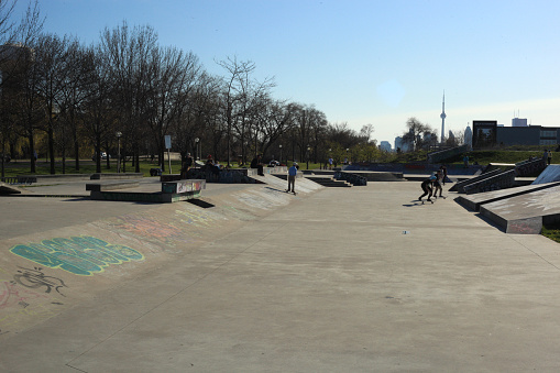 Toronto, Сanada- May 6, 2016: Horizontal image of people skateboarding on outdoor skateboard park, near woodbine beach, with CN Tower in far right background. 