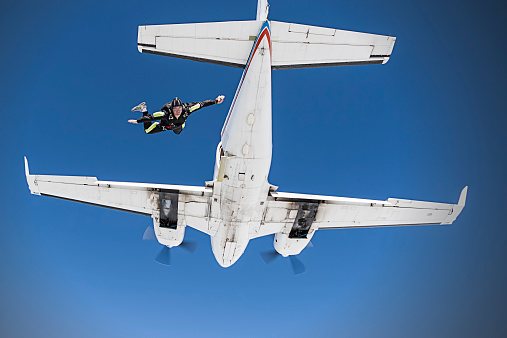 A skydiver a split second after jumping from a dual engine airplane against a bright blue sky.